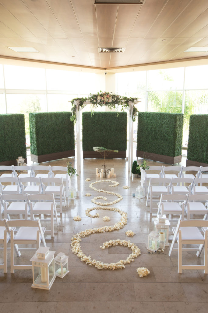 A modern wedding color theme of greens and ivories. Flowers line the aisle in beautiful swirls as they lead to an arch with greenery on the top.