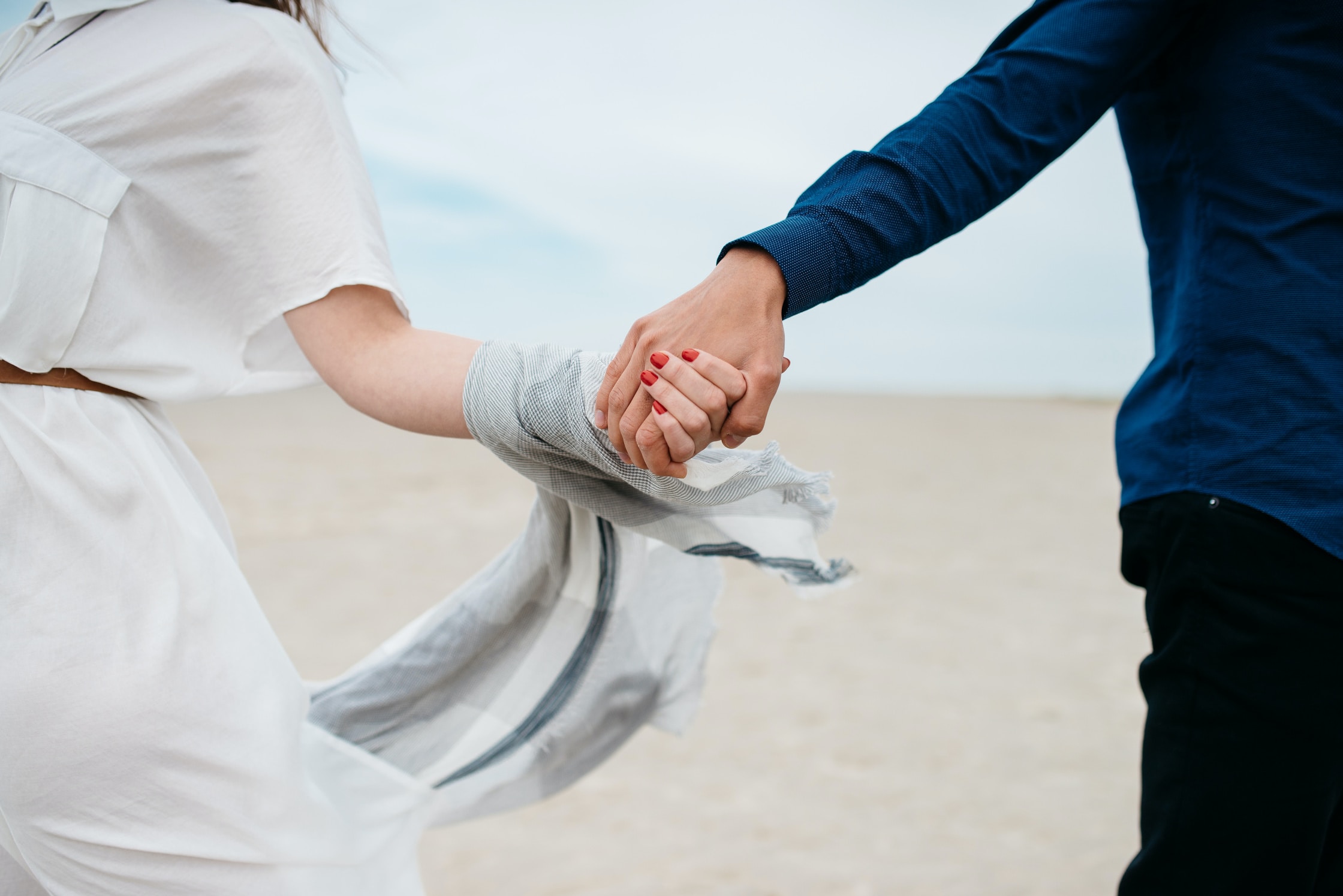 A newly engaged couple walking on the beach holding hands. In the frame is just of the arms reaching out and holding hands.