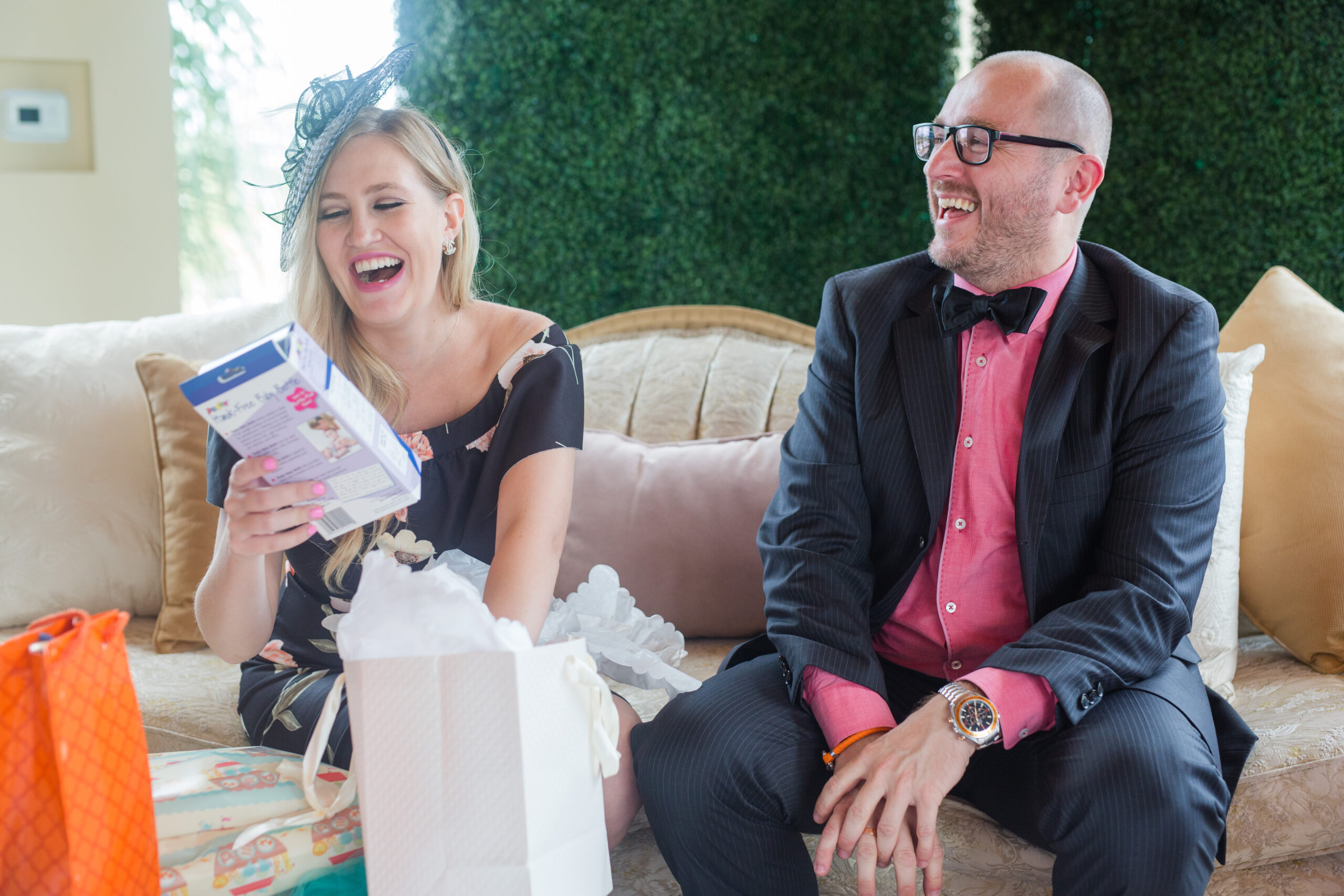 A couple celebrating their Alice in Wonderland-themed baby shower at The Centre Escondido. They are opening gifts and laughing.