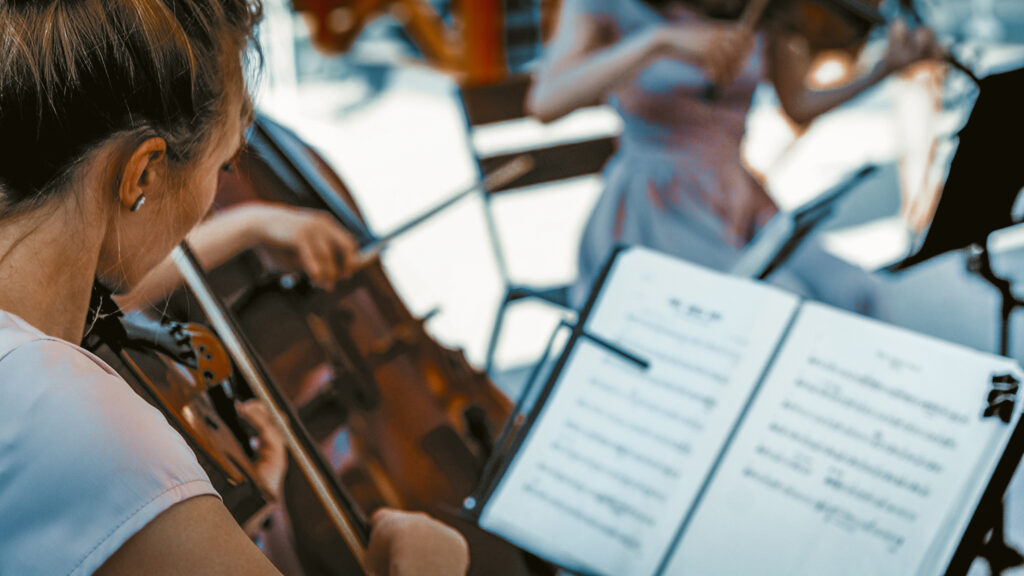 Classical Music themed Event with young woman Playing Violin And Looking At Score Dressed Up In Lilliak Classical Dresses