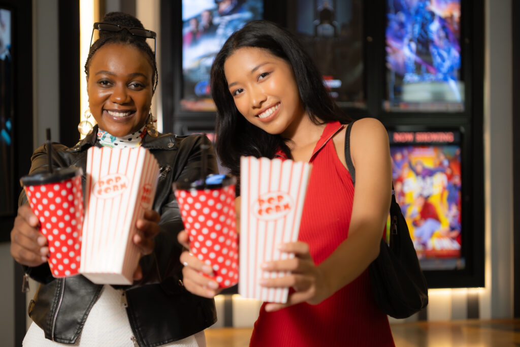 Two ladies eating popcorn and drinking glass a companion item of people for watching movies at the holiday movie party