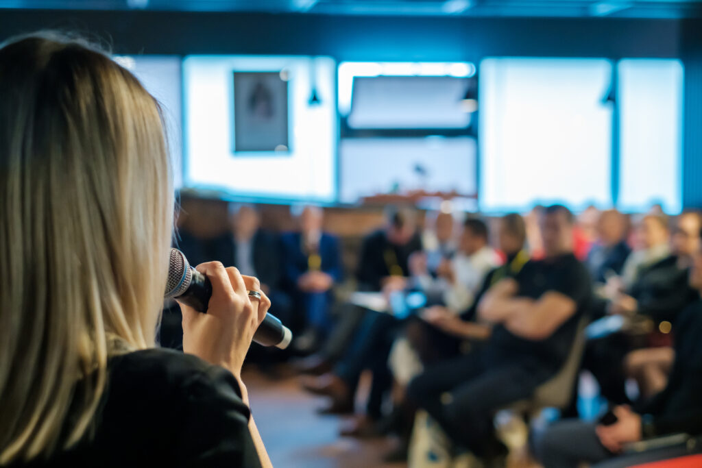 Female presenter speaks to audiences at event open mic.