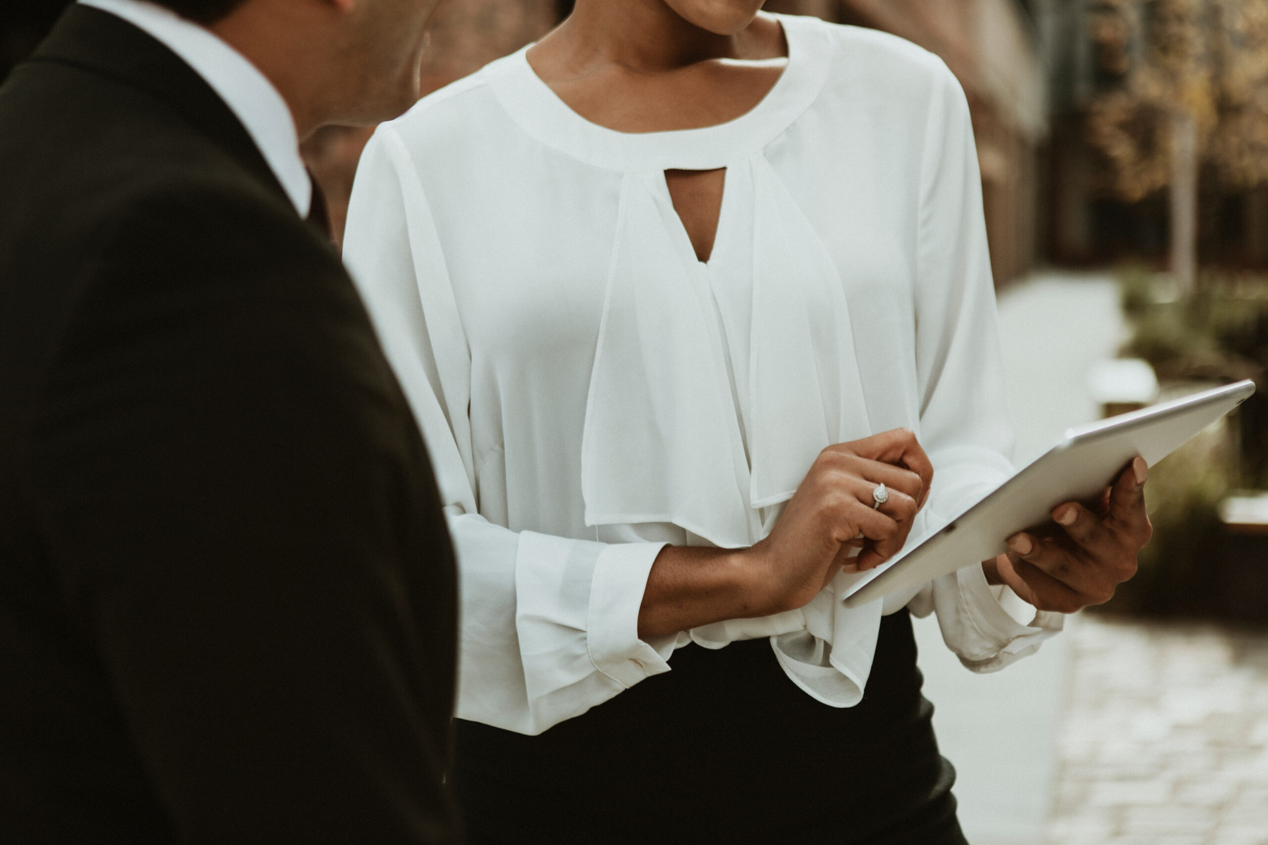 Wedding planner using a tablet with the wedding reception plan. She is standing with a man in a tux, we see his back and assume him to be a part of the wedding couple.