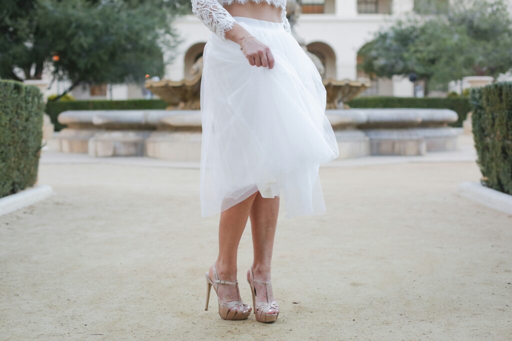 A shot of a brides wedding dress set. You can see her skirt and beautiful metallic shoes, and the bottom of her shirt which is a beautiful laced crop top.