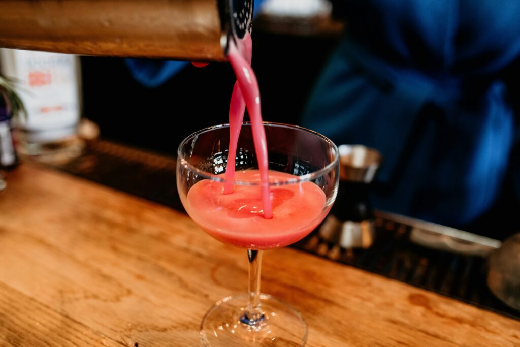 A closeup of a cocktail being made. It looks beautifully pink and is being poured from a silver cocktail shaker.