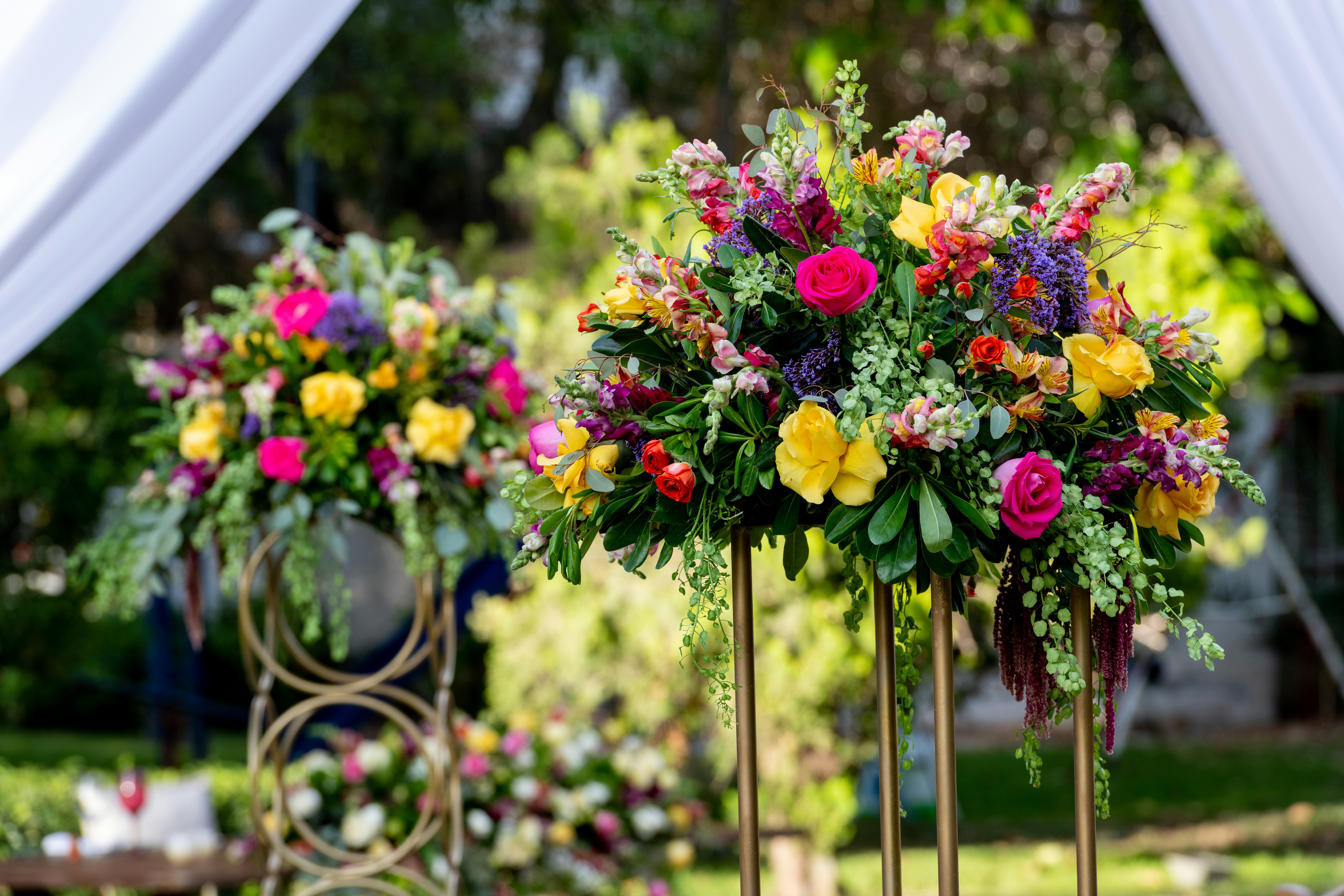 A closeup of two architectural floral arrangements. They are very colorful and sitting atop a structure of brass.
