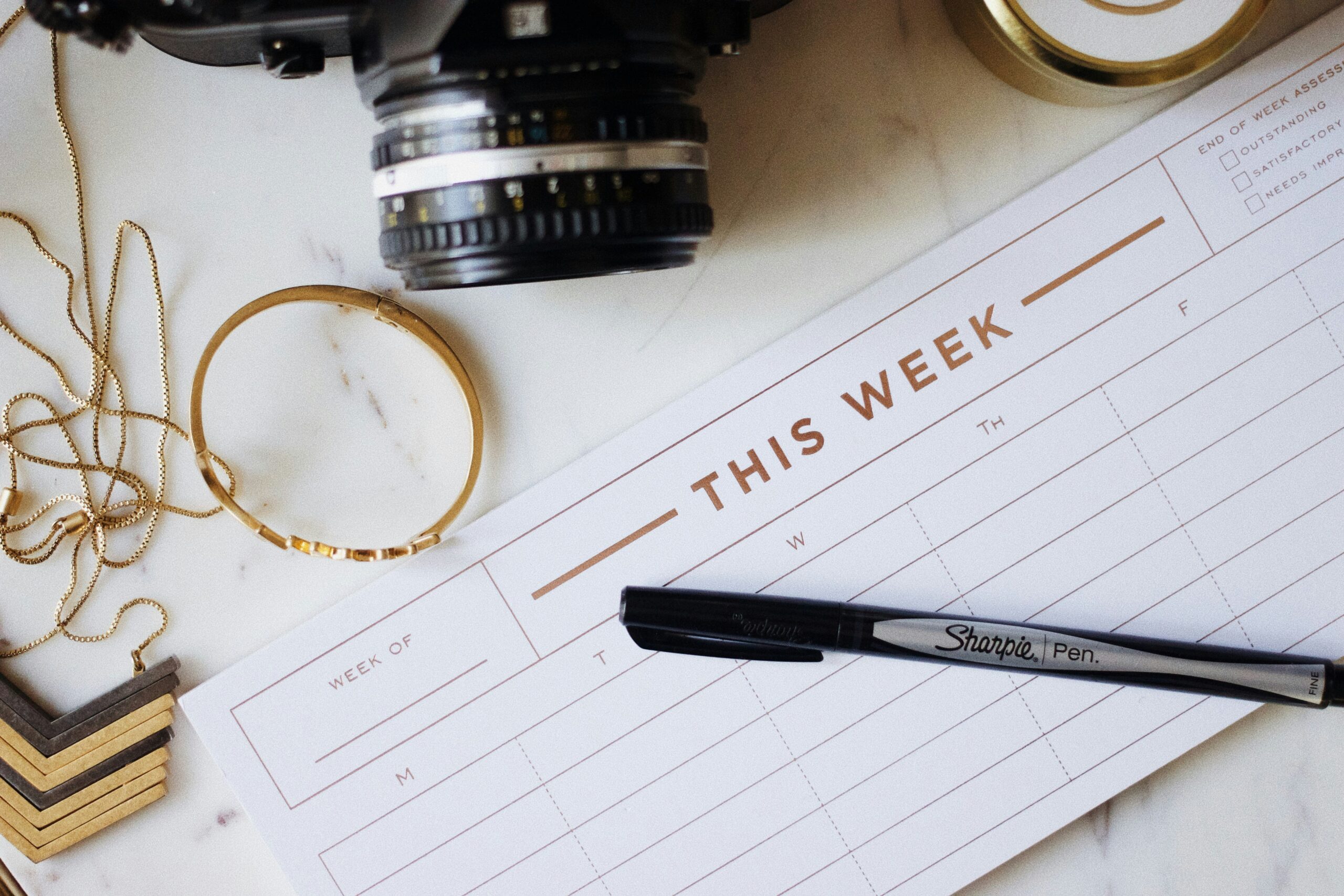 A free wedding tool, this week's tasks, alongside a camera and pen on a marble table.