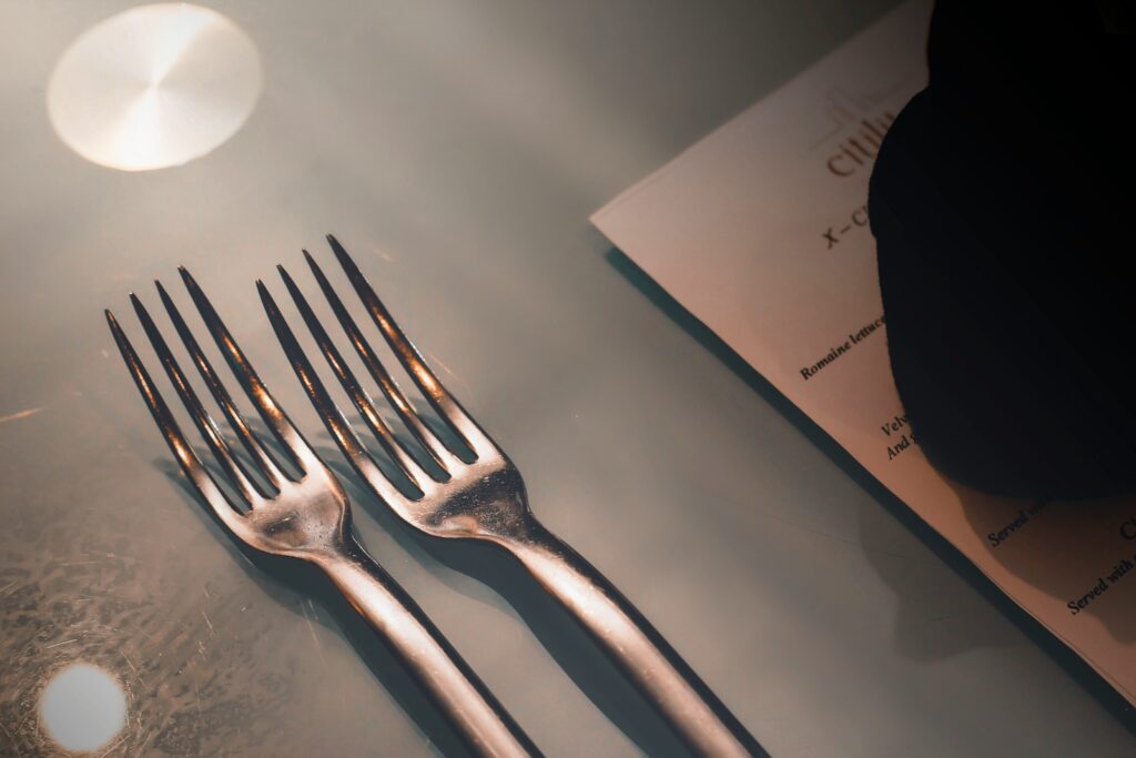 A menu on a table setting with forks in the forefront for a holiday party menu